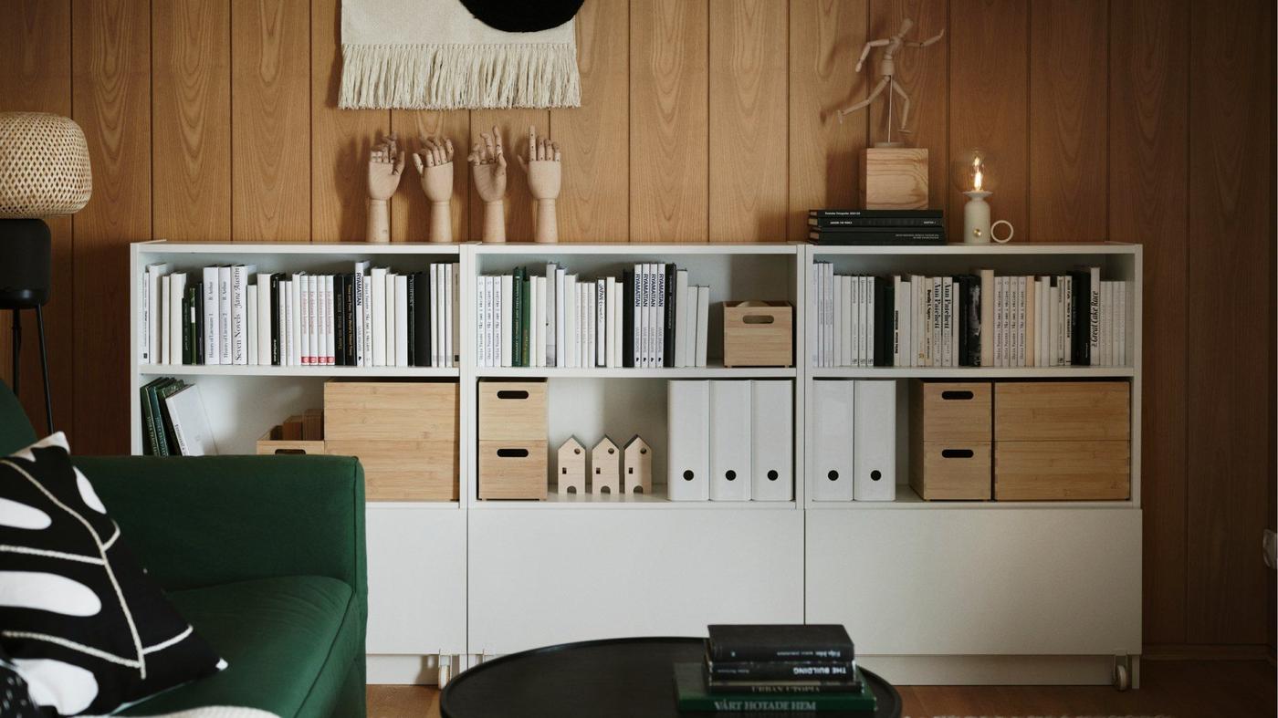 Several white BILLY bookcases against a wood-panelled wall. The shelves are filled with books, boxes and wooden sculptures.