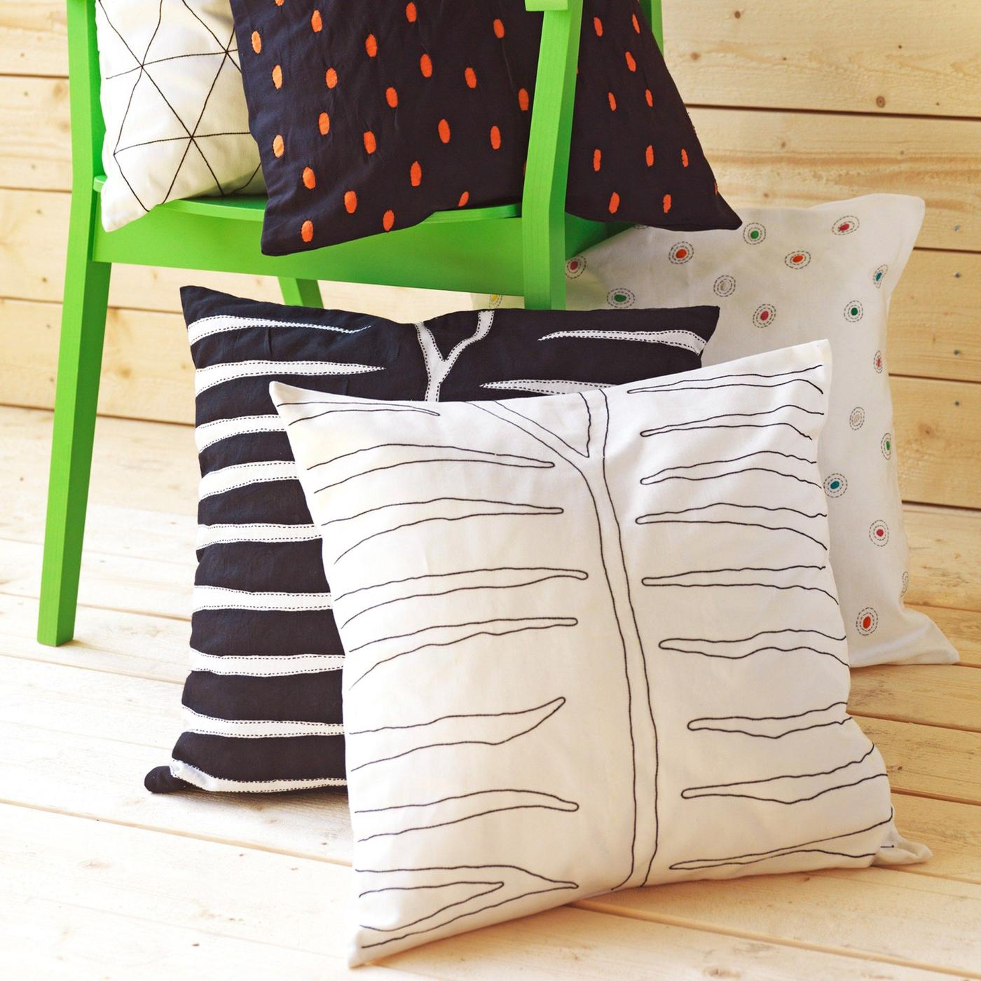 Two cushions with hand-embroidered cushion covers with zebra patterns on a wooden floor, leaning against a green chair.