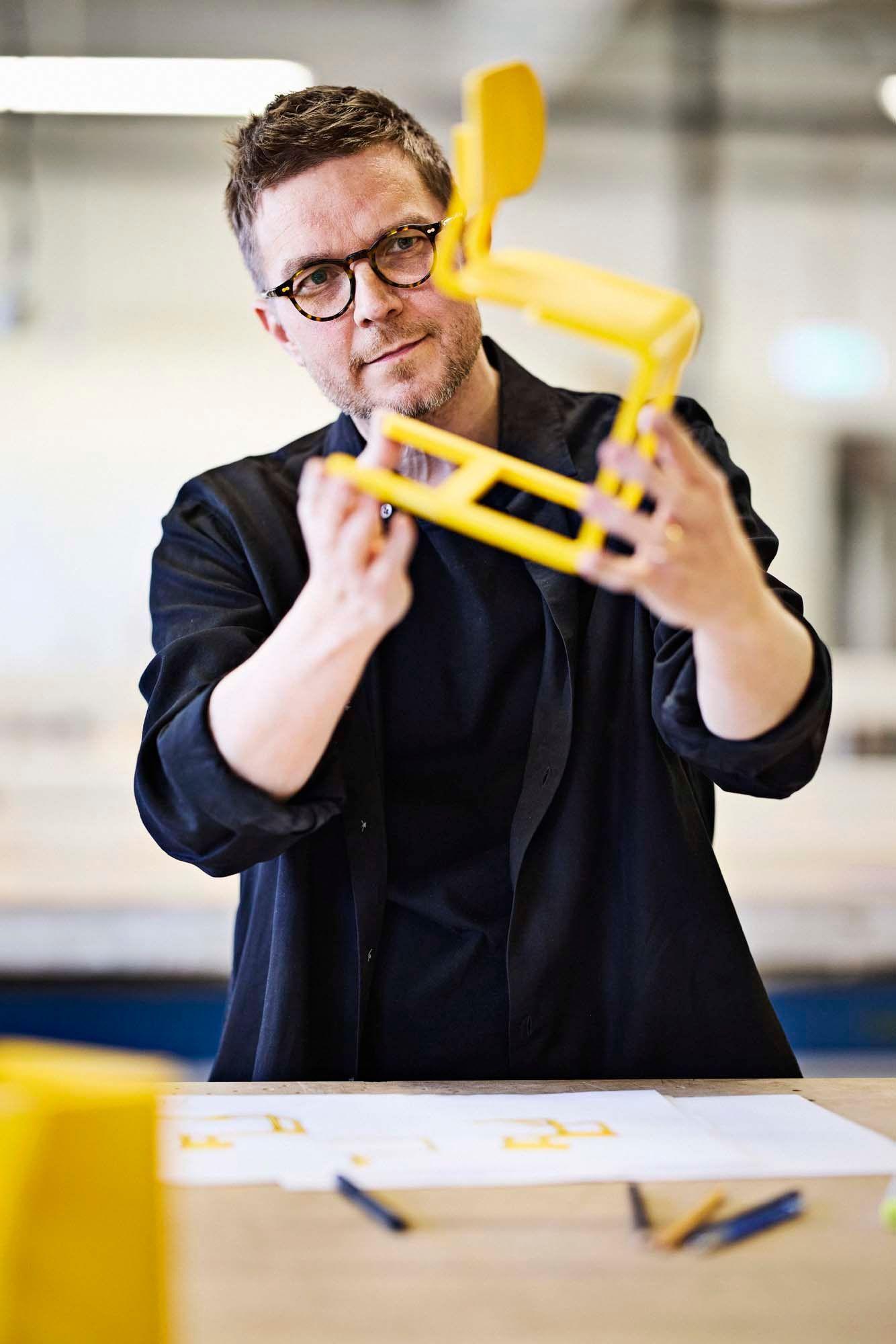 IKEA designer Henrik Preutz holds up a small model of a yellow LYCKAN chair. 