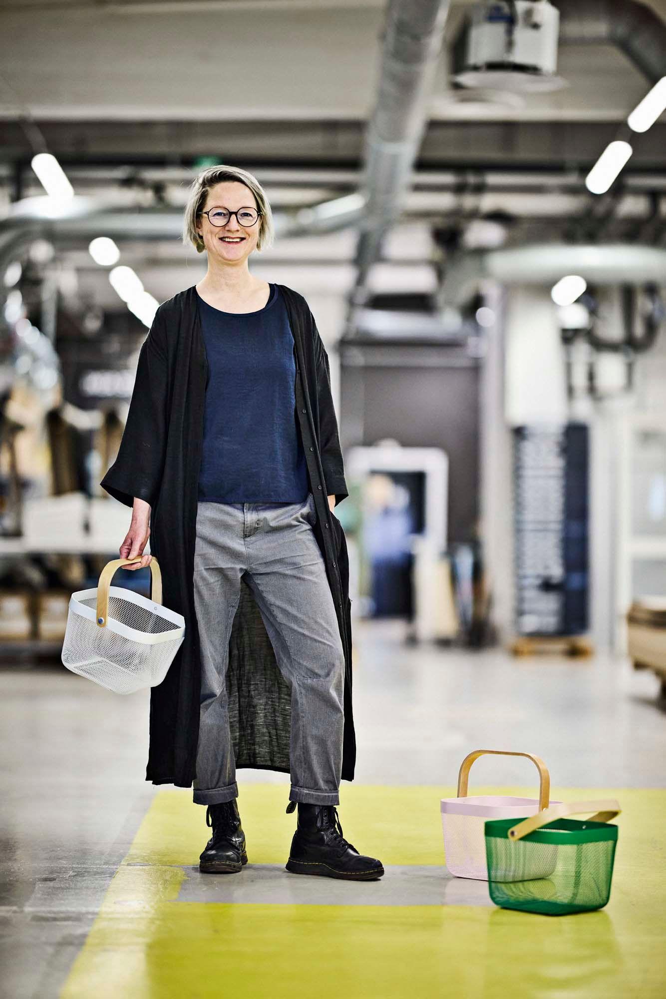 IKEA designer Wiebke Braasch smiles while standing and holding a white RISATORP basket in her right hand.