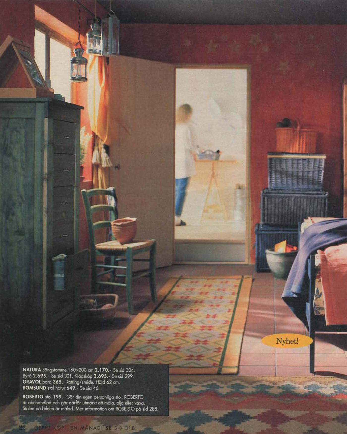 A bedroom with stencilled decoration on the wall. The door is open, revealing a person in another room in the background.