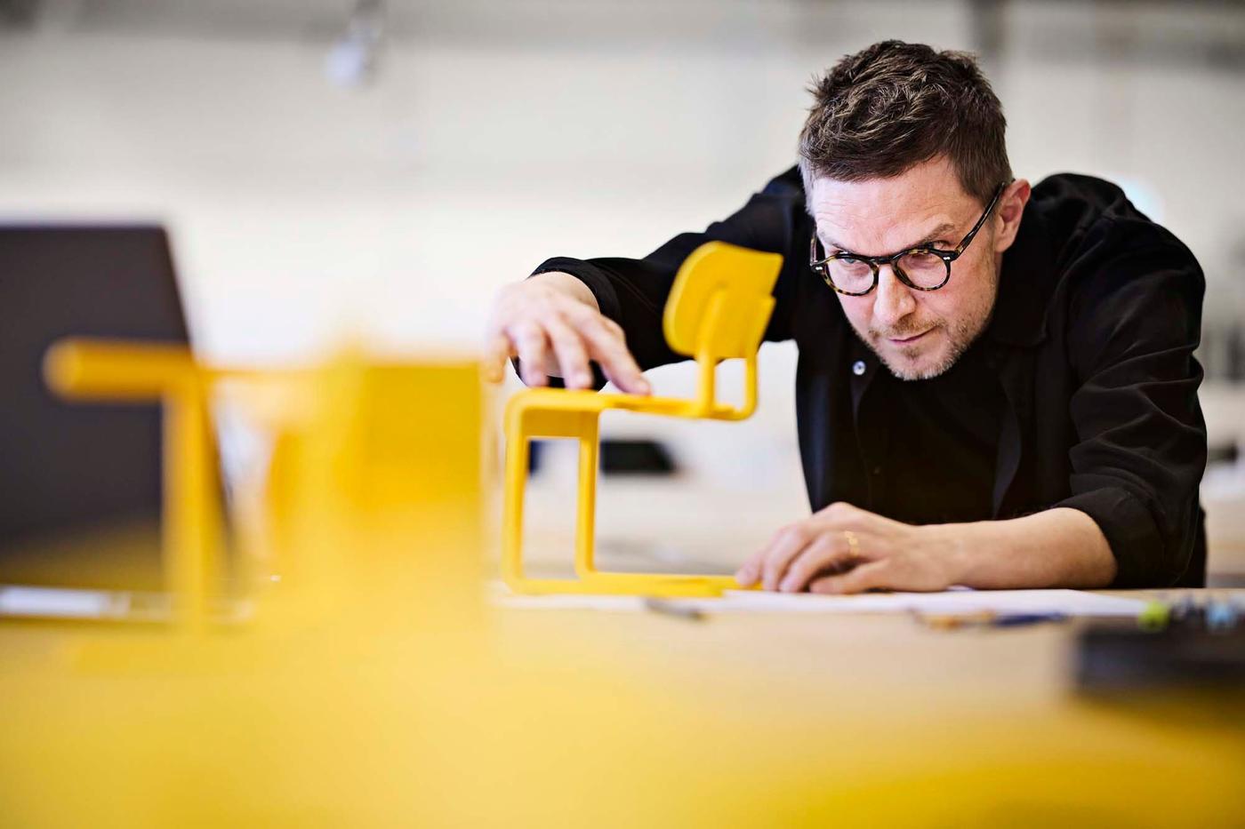 IKEA designer Henrik Preutz examines a model of a yellow LYCKAN chair.