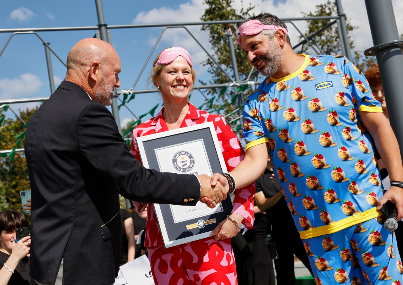 A woman in red pyjamas in standing with a framed certificate and man in blue pyjamas is shaking the henad of a Guinness world records representative