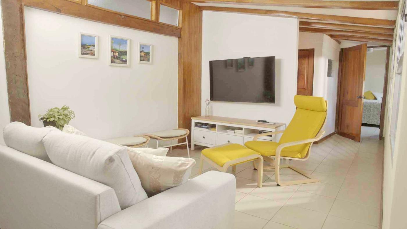 A living room with a yellow chair and footstool in front of a wall-mounted TV.
