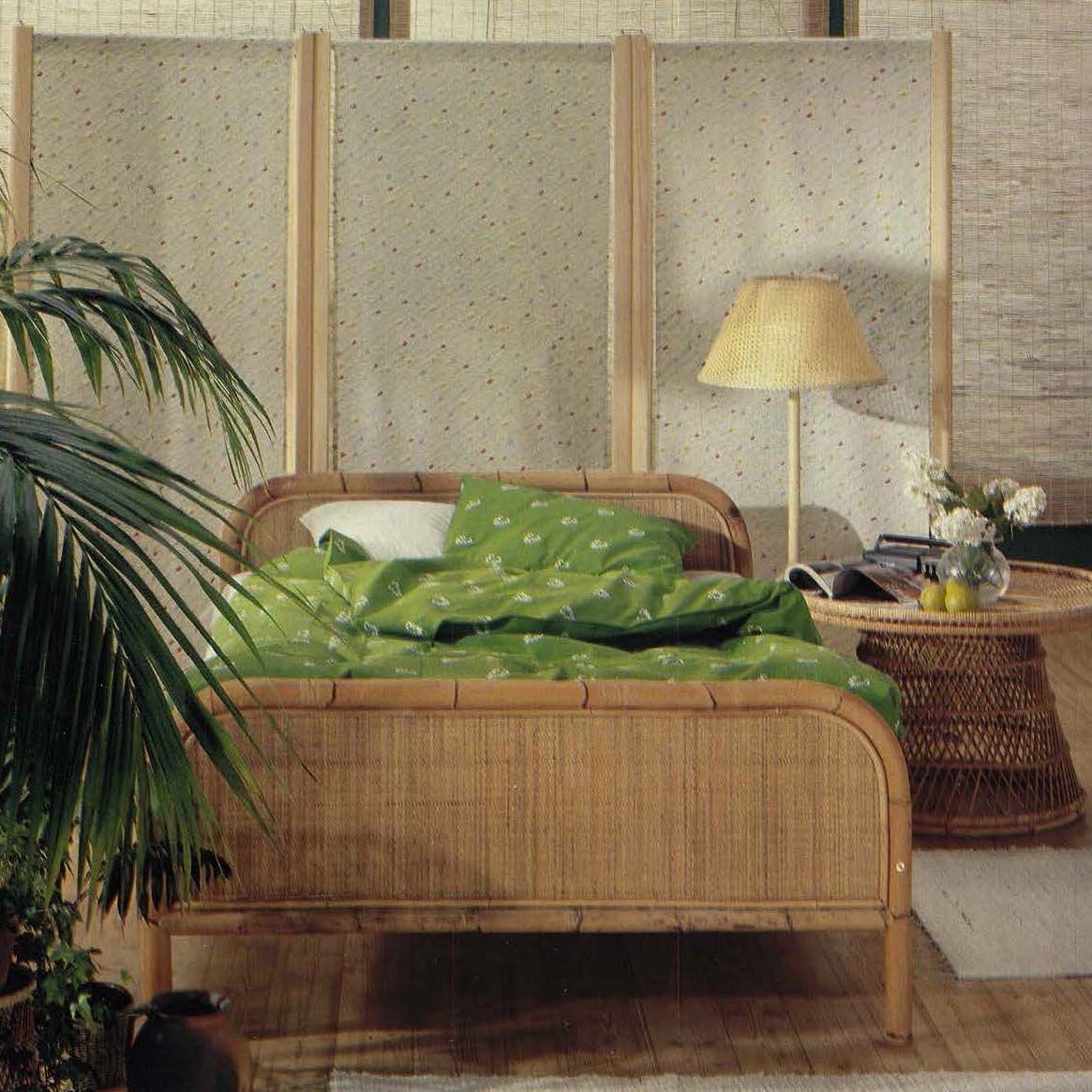 The 1980 IKEA catalogue showing a bamboo bed with green bedlinen in a bedroom. There is a large plant.