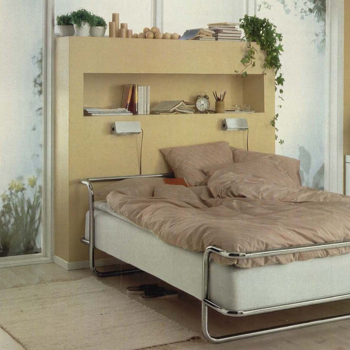 The 1982 IKEA catalogue, showing a metal bed with beige bedlinen and a large cream headboard/storage unit behind.