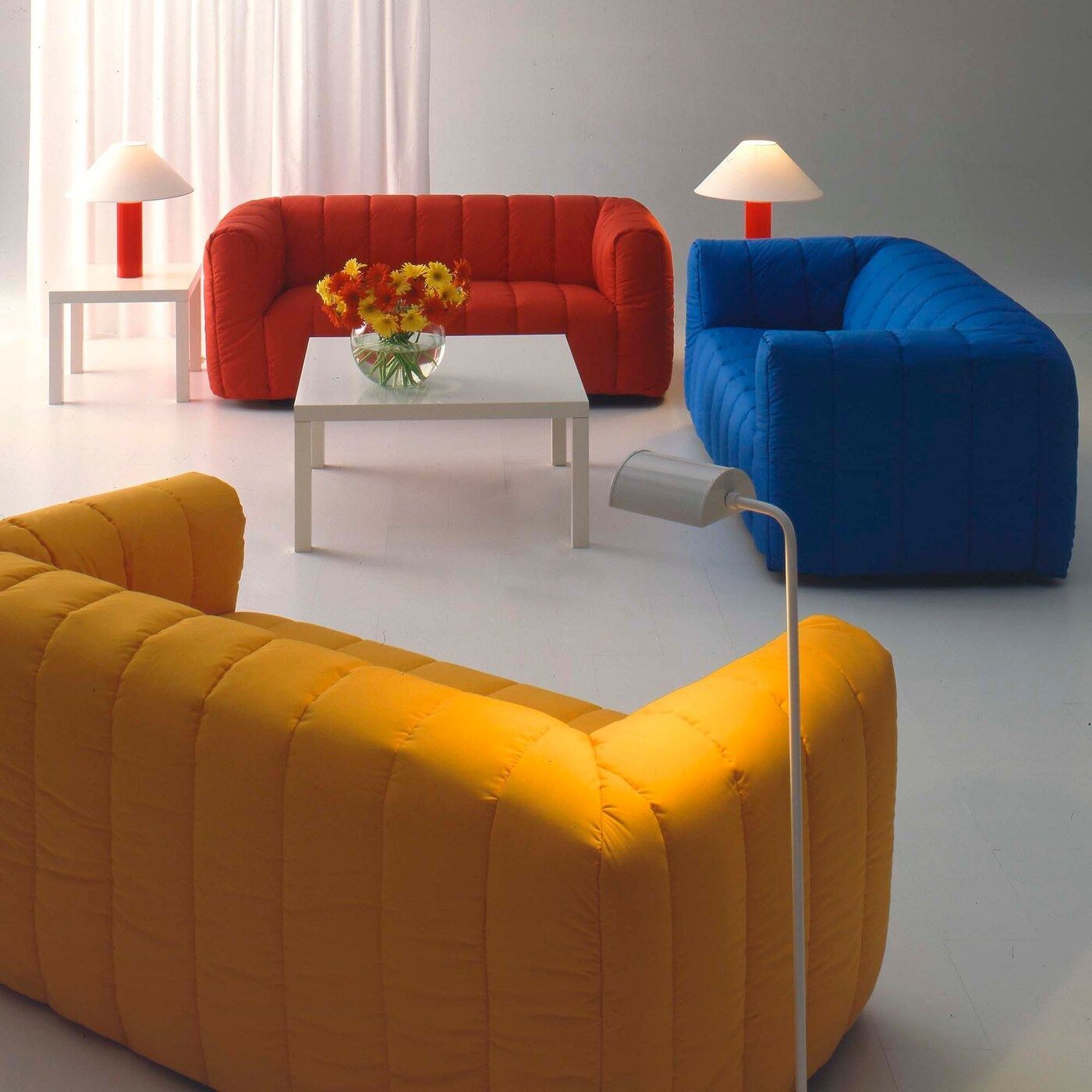 Three KLIPPAN sofas in yellow, blue and red in an ultra contemporary '80s room set.