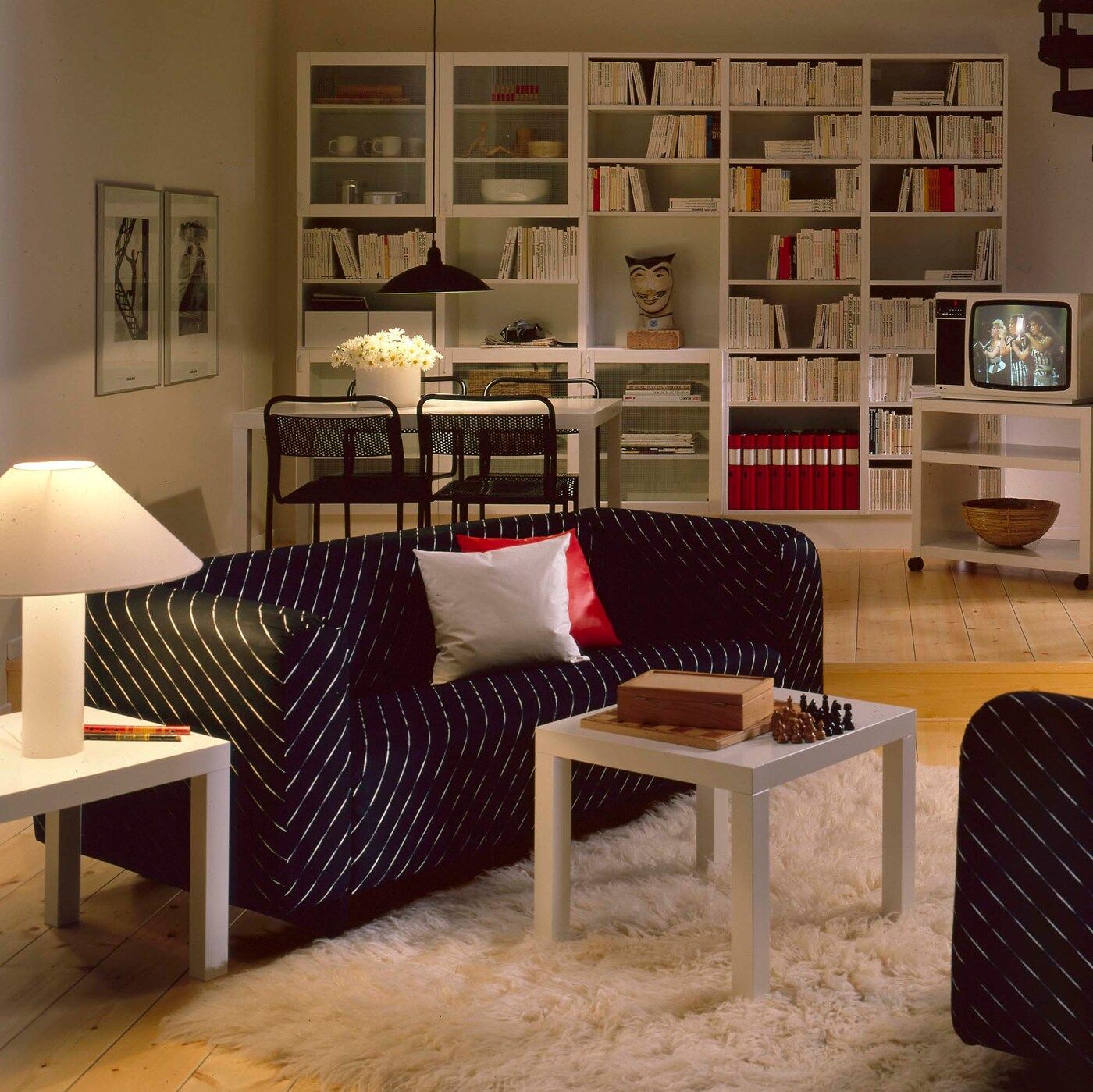 A black pinstripe KLIPPAN sofa in a cosy living room with warm, dimmed lighting and large bookcases.