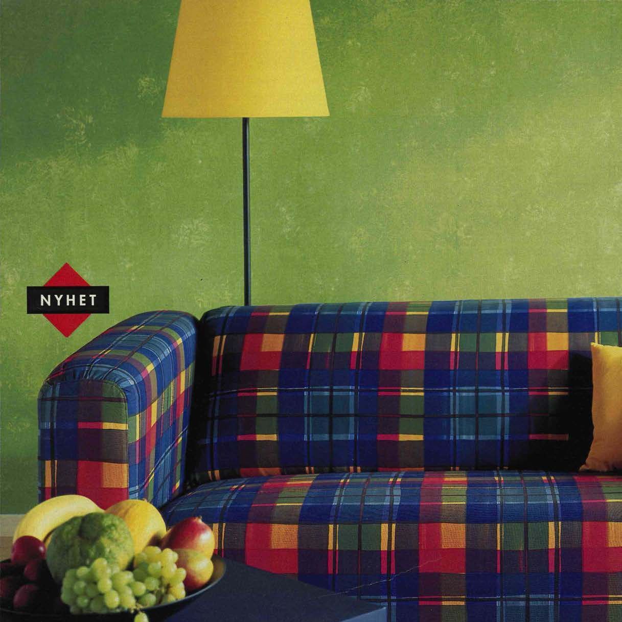 KLIPPAN sofa with blue, red, green and yellow checked pattern against lime green wall with a bowl of fruit on a table in the foreground.