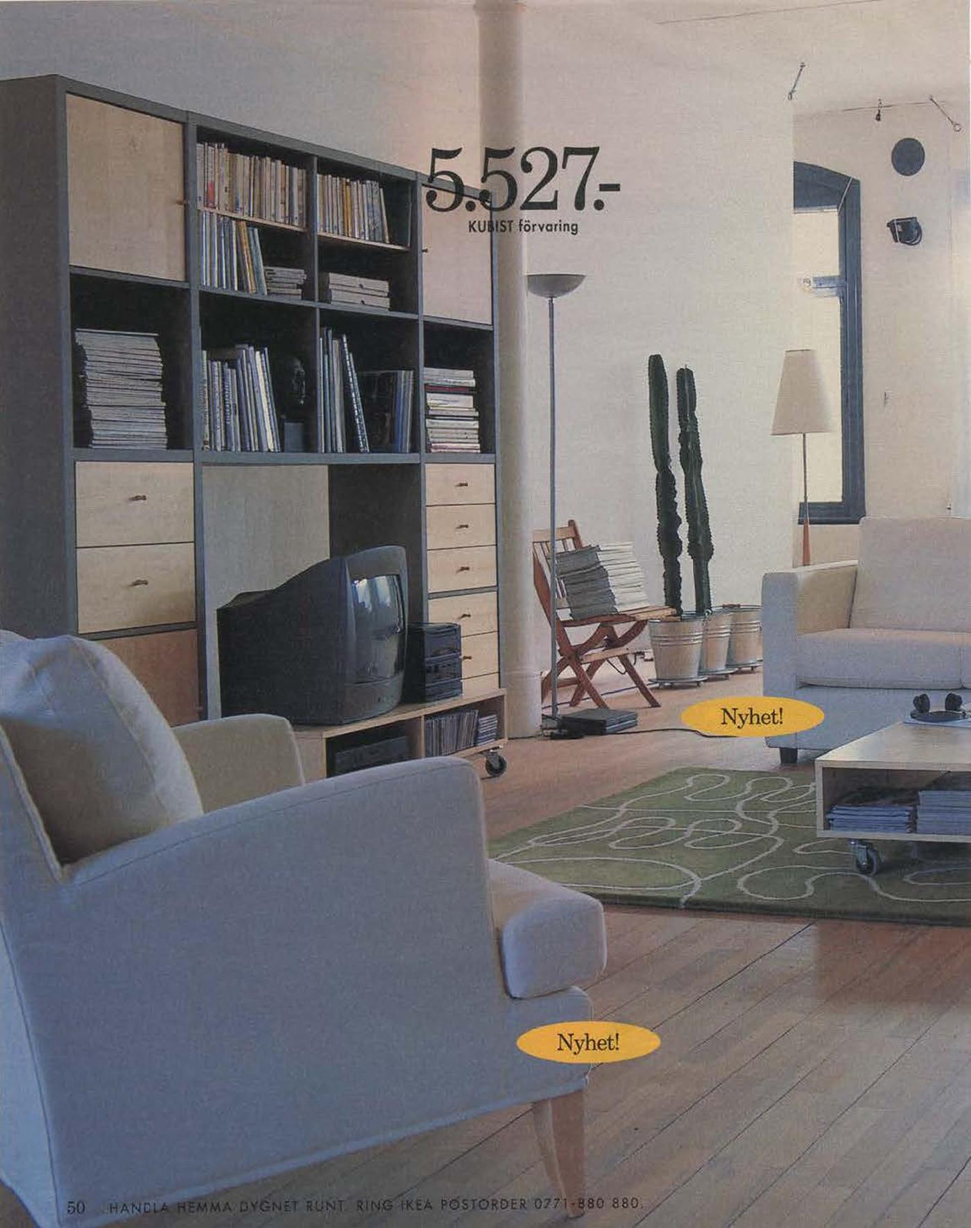 A light living room setting with a blue chair and a tall grey and wood wall unit with a TV, magazines and books.