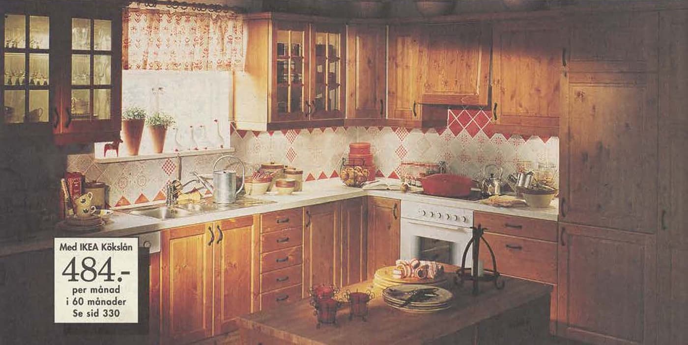 A kitchen from the 1996 catalogue featuring wood REJÄL cupboard units above and below the crowded countertop.