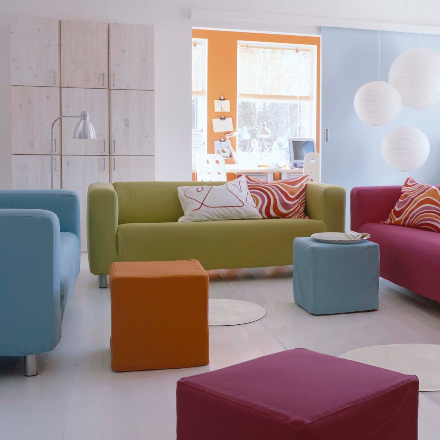 Three KLIPPAn sofas in light blue, green and pink in a minimal white room.
