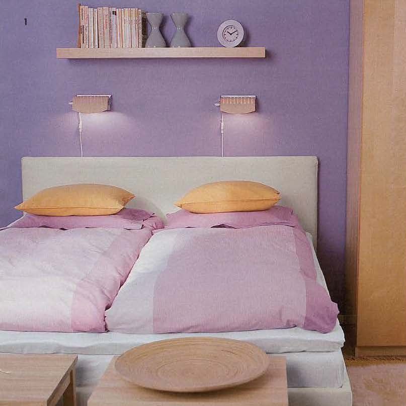The 2002 IKEA catalogue featuring a lilac bedroom with a double bed with two single duvets in lilac. There are two illuminated lamps and a bookshelp above the bed.