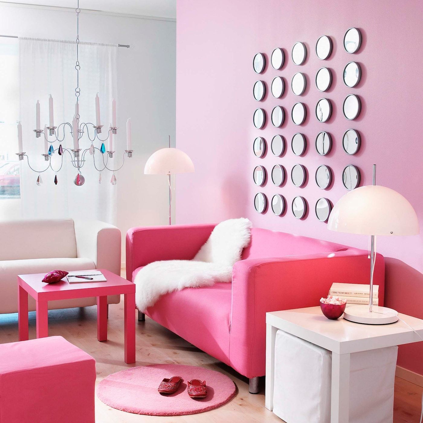 A bright pink KLIPPAN sofa in a pink living room, against a wall of 25 small clocks arranged in a square.