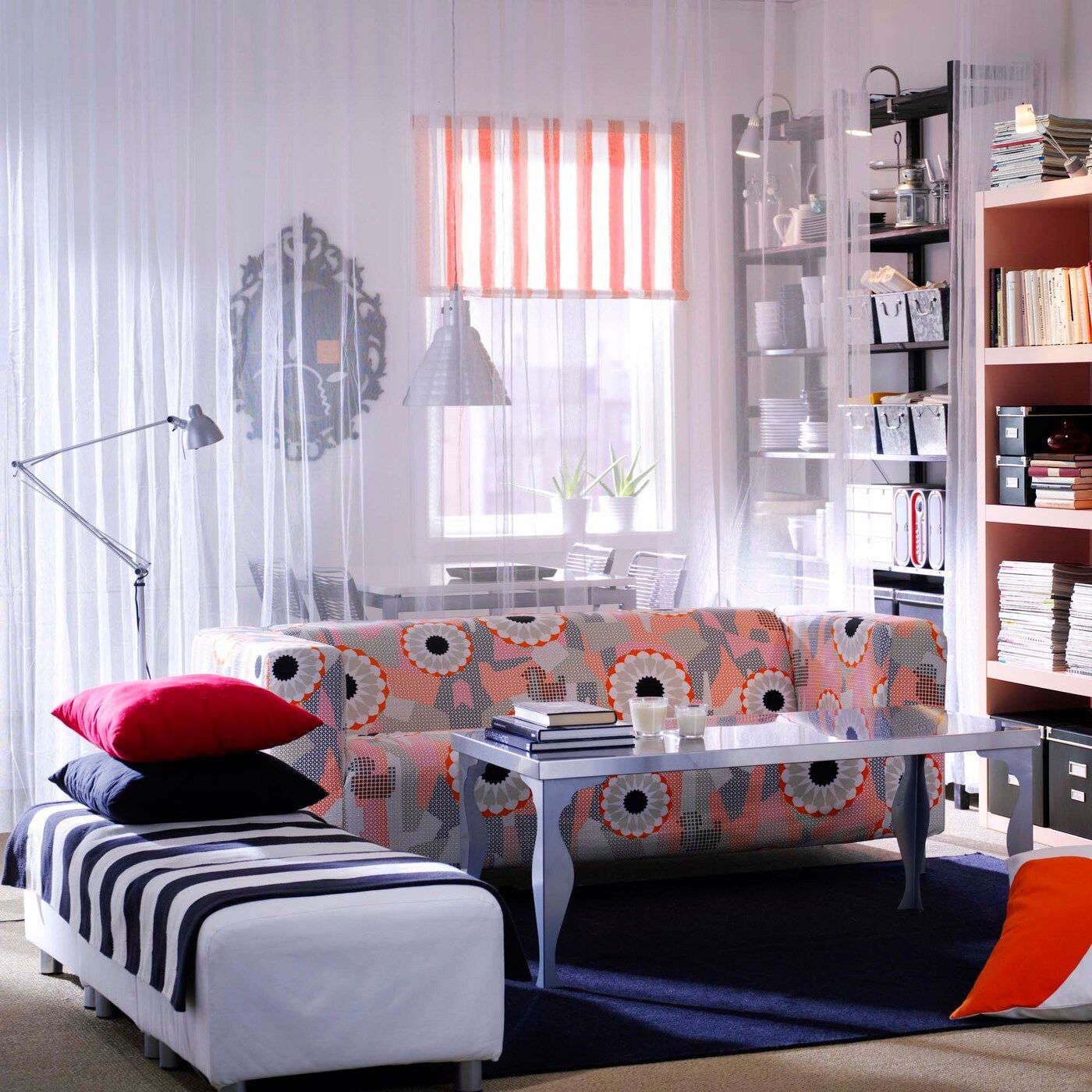 A sheer curtain separates a living room with a modern floral patterned KLIPPAN sofa from a dining area.