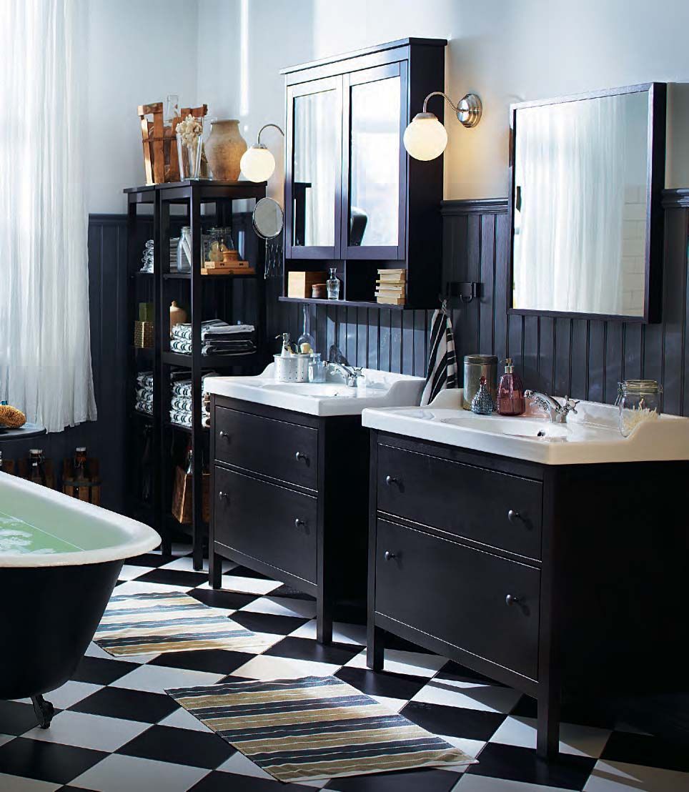 A black and white bathroom with two vanity basins with black units. The floor is chequerboard tiled.