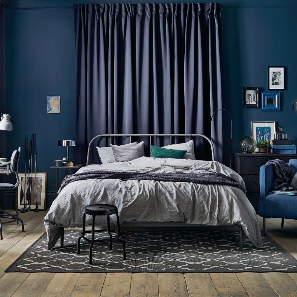 The 2018 IKEA catalogue shows a roomset showing a blue metal frame bed with blue and grey bedlinen. Behind the bed are drawn blue cutrains and a blue chair is placed on the right. 