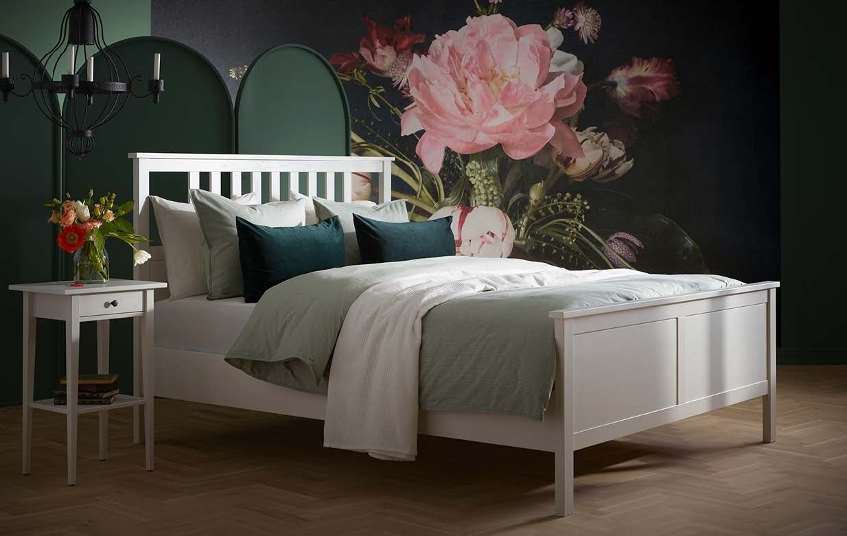 A dark green bedroom with a white bed from the 2020 IKEA catalogue. On the wall there is a giant image of flowers.
