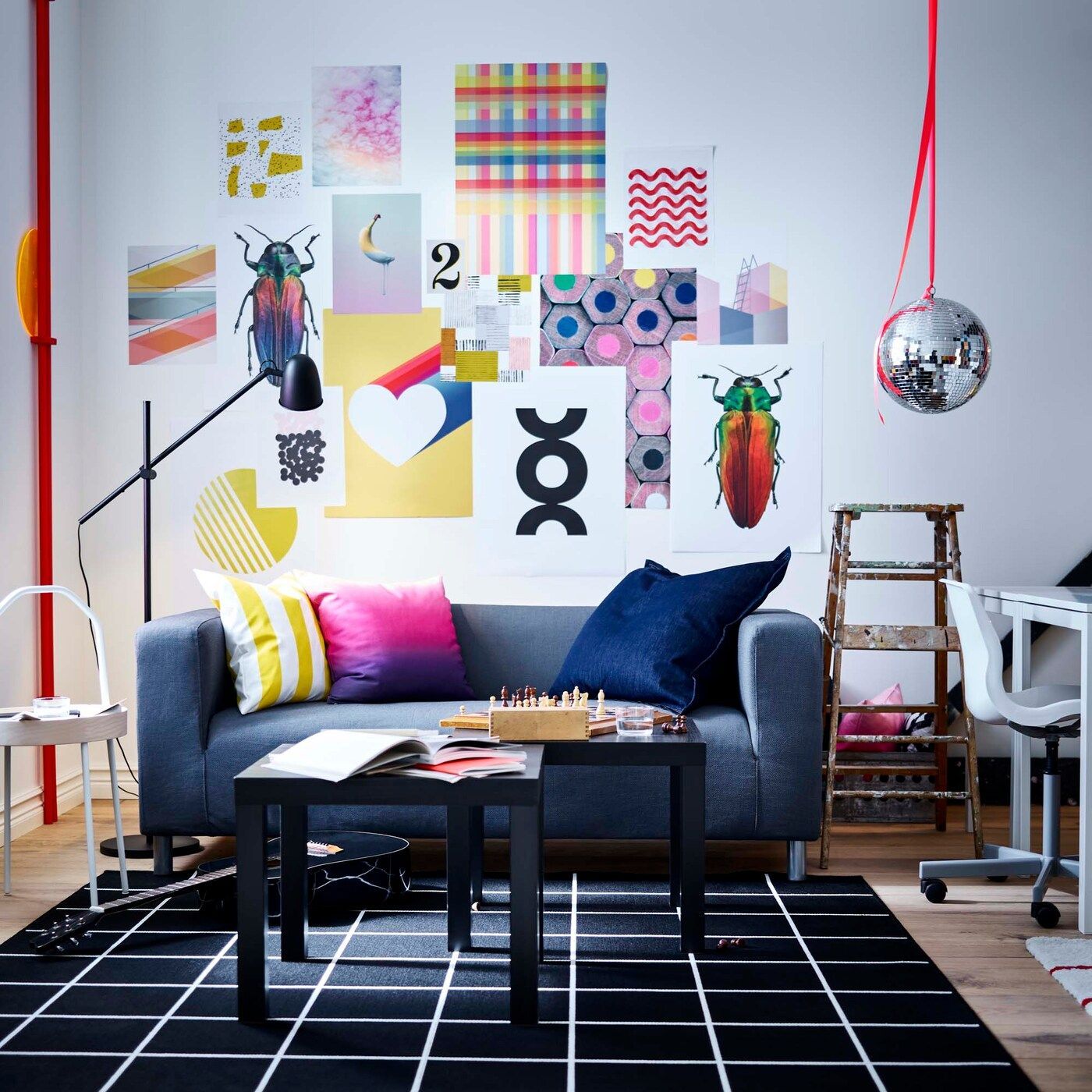 Grey KLIPPAN sofa against a wall with bold, playful prints and posters collaged on the wall behind.