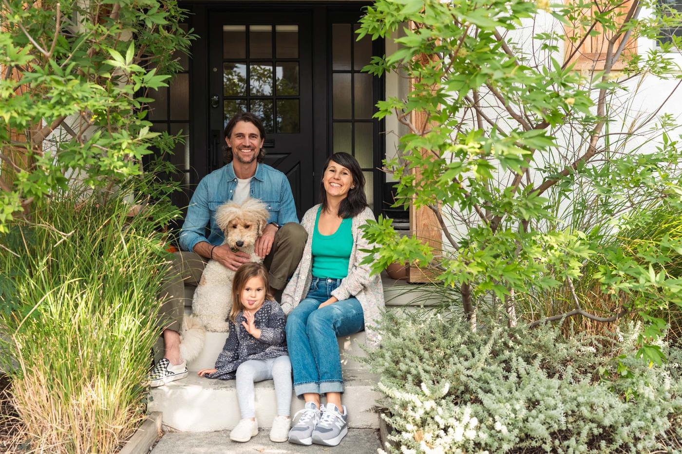 A family with a dog sitting on their porch in front of a black door.