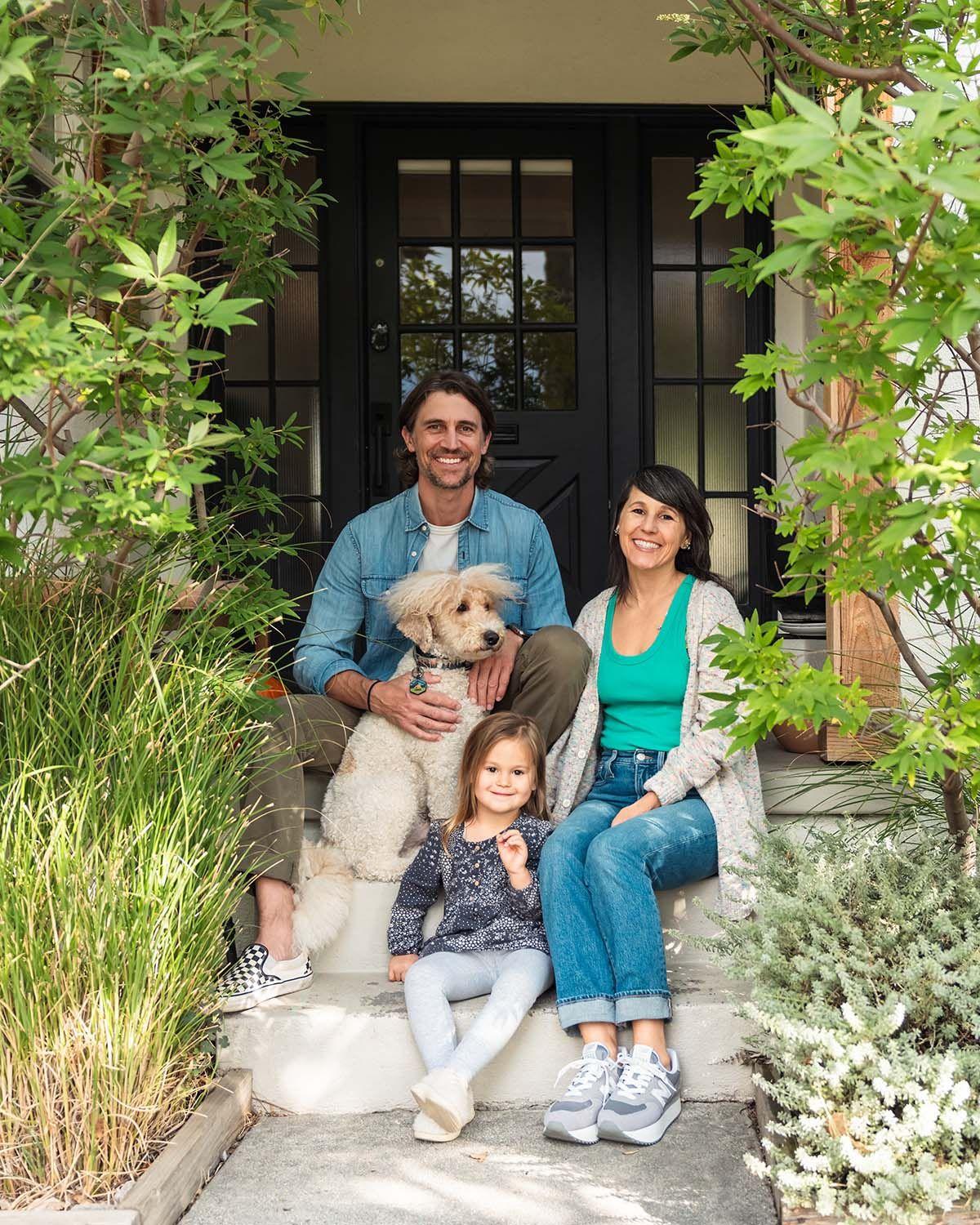 A family who are participants in the 50L Home Coalition project sit together on the front steps of their house.