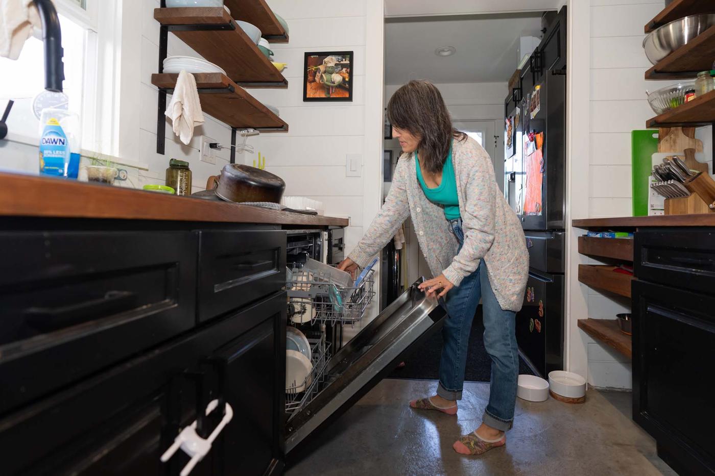 A person loading the dishwasher in a black, white and wood kitchen.