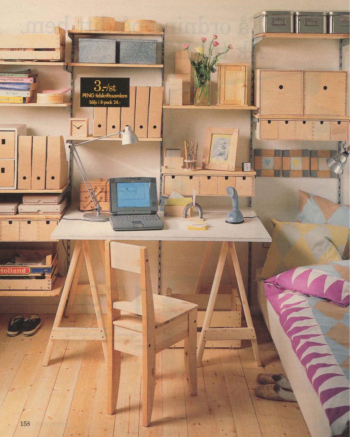 A wooden desk, chair and storage in a home office in the 1996 catalogue. On the desk is a small laptop computer.