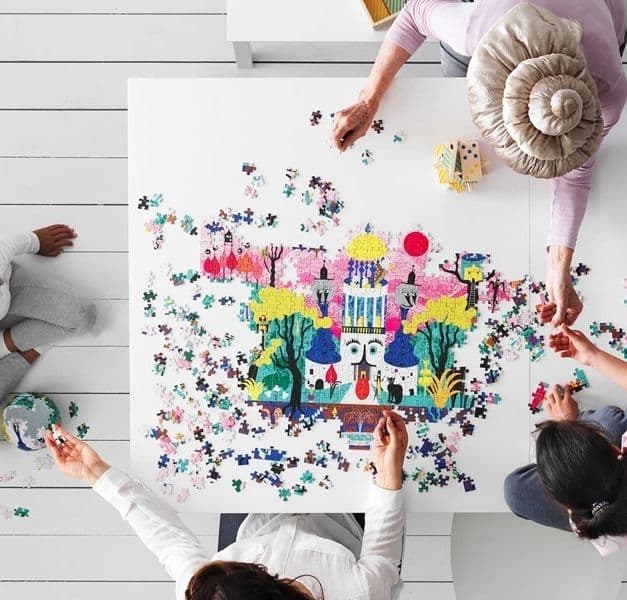 Overhead view of a group of people assembling a colourful jigsaw puzzle on a white table.