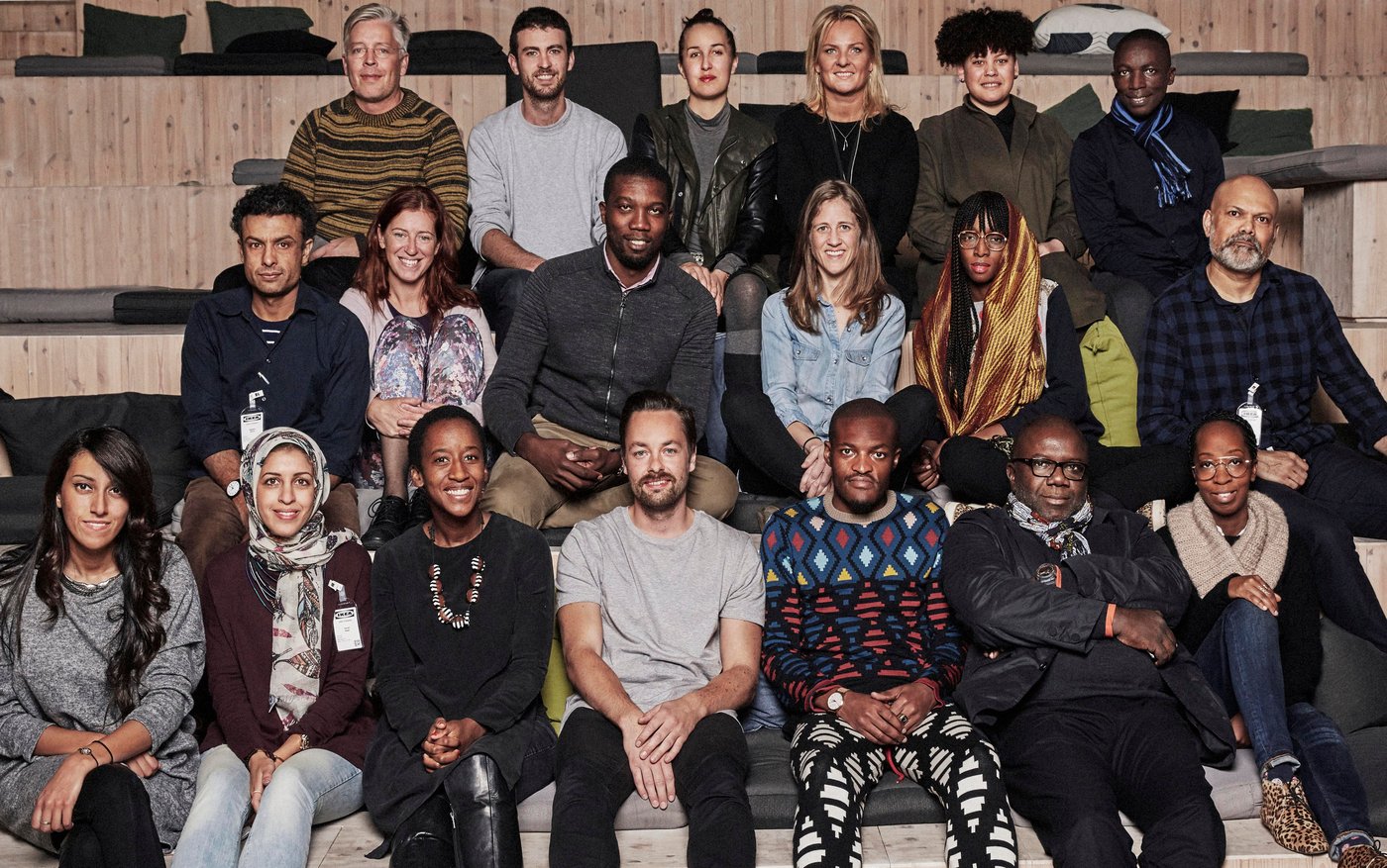 A group of men and women sit. they are all looking at the camera.