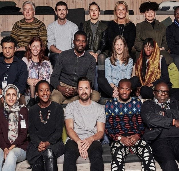 A group of men and women sit. they are all looking at the camera.