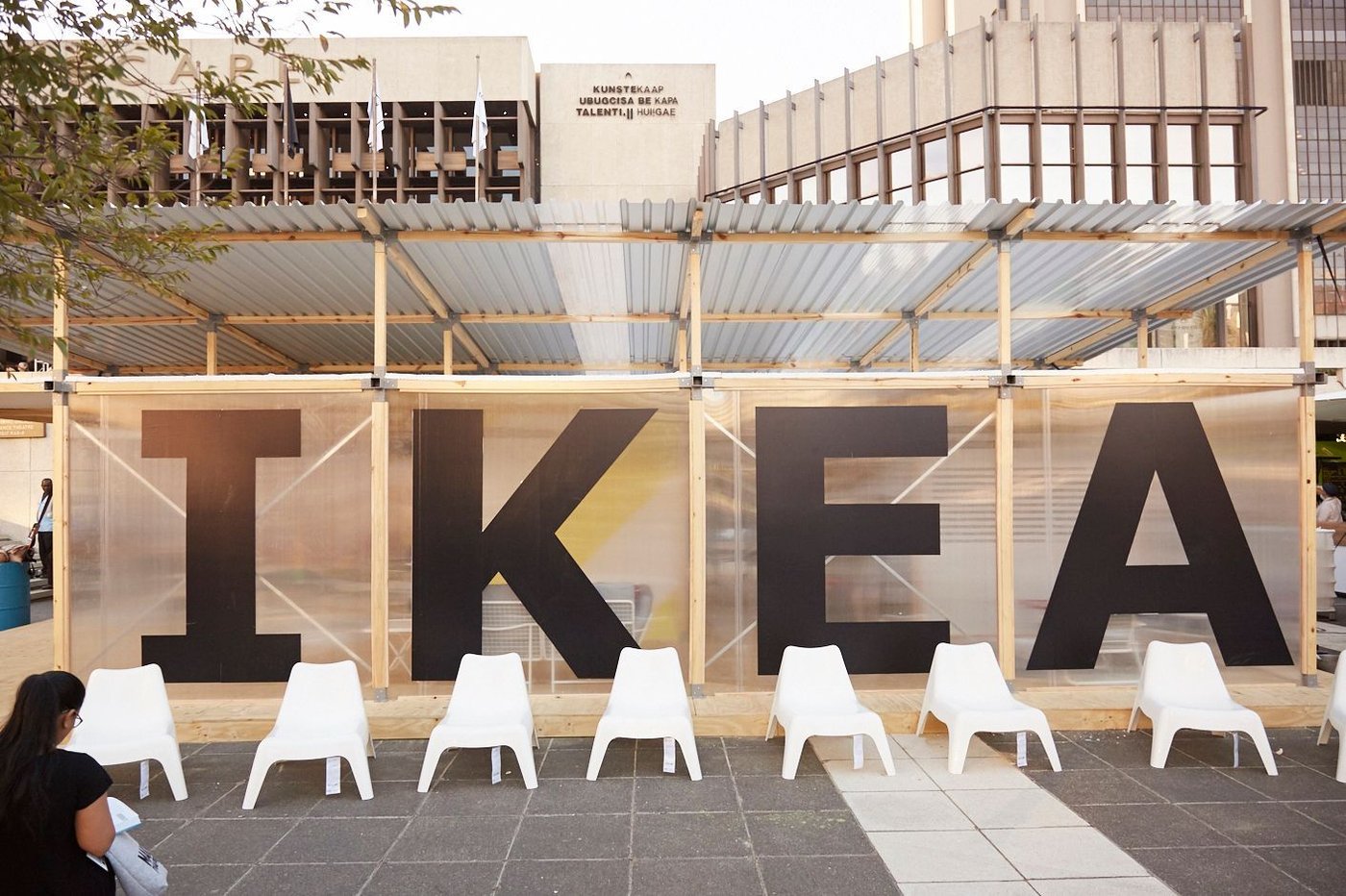 An IKEA sign with white chairs in front of the sign.
