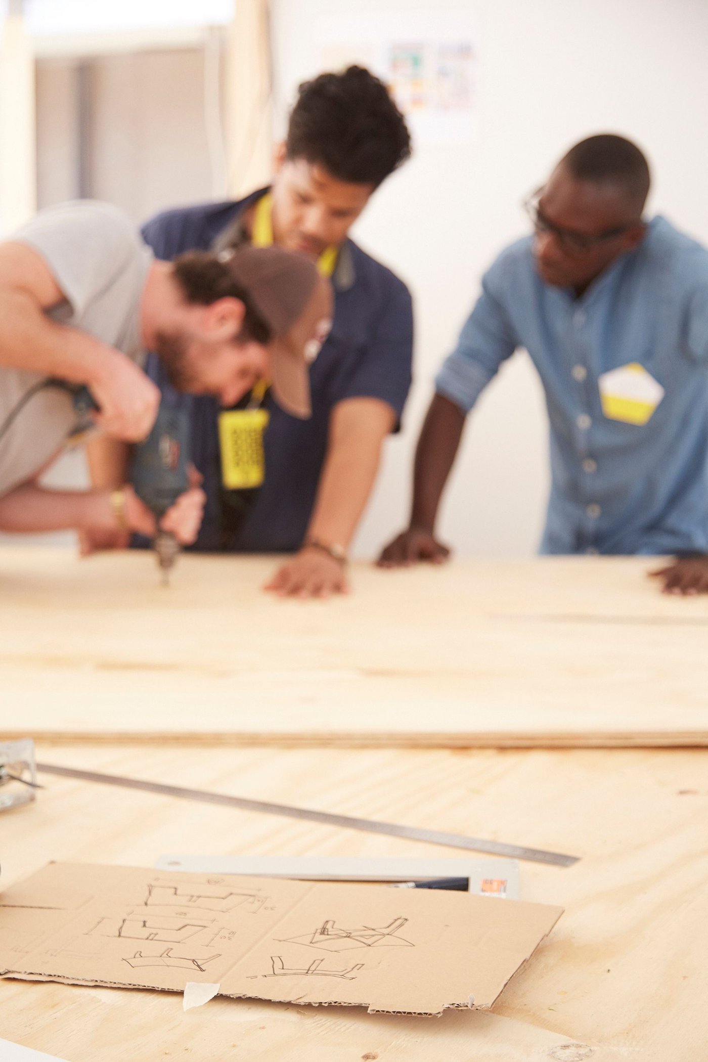 Two men watch another man using an electric tool.