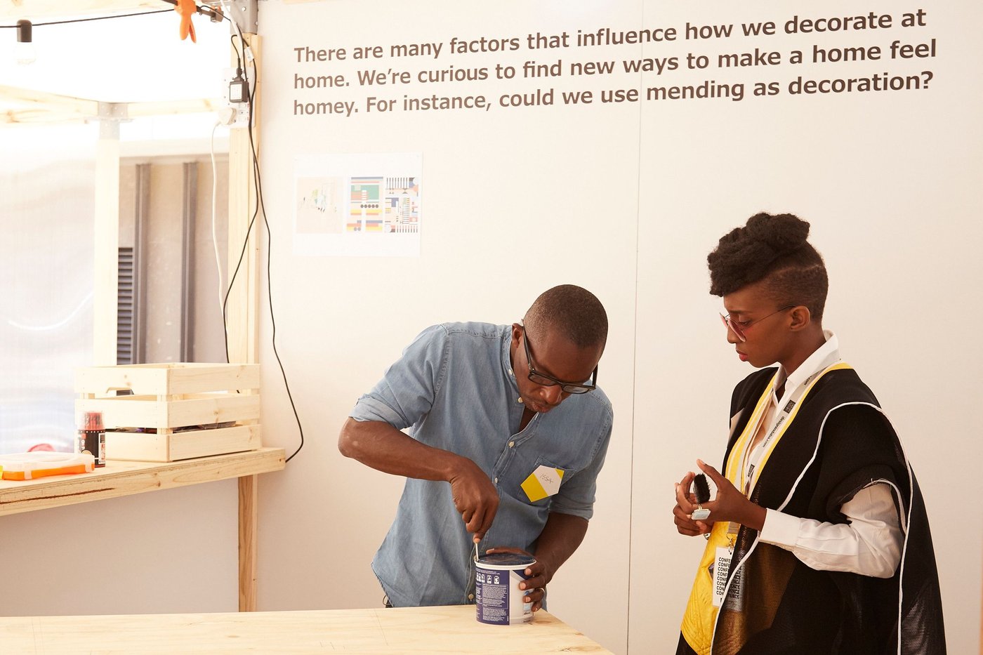 A woman watches a man trying to open a tin with a screwdriver.