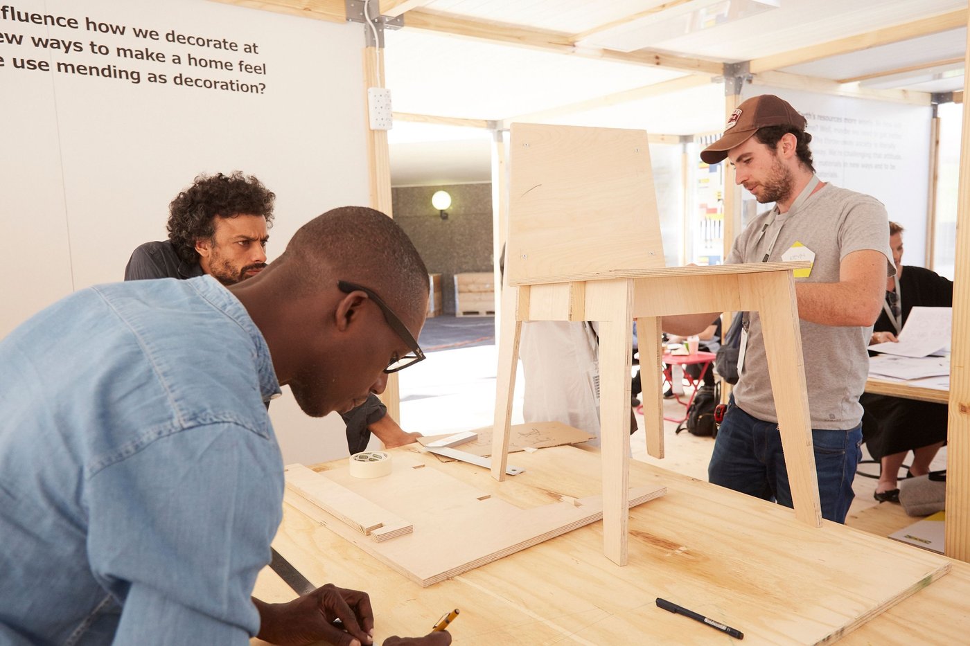 A person constructs a table while another person looks and a third person draws.