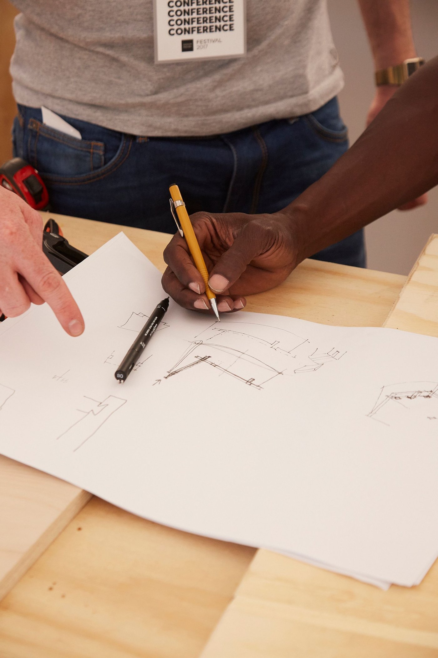 A person sketches, while another person holds the paper.