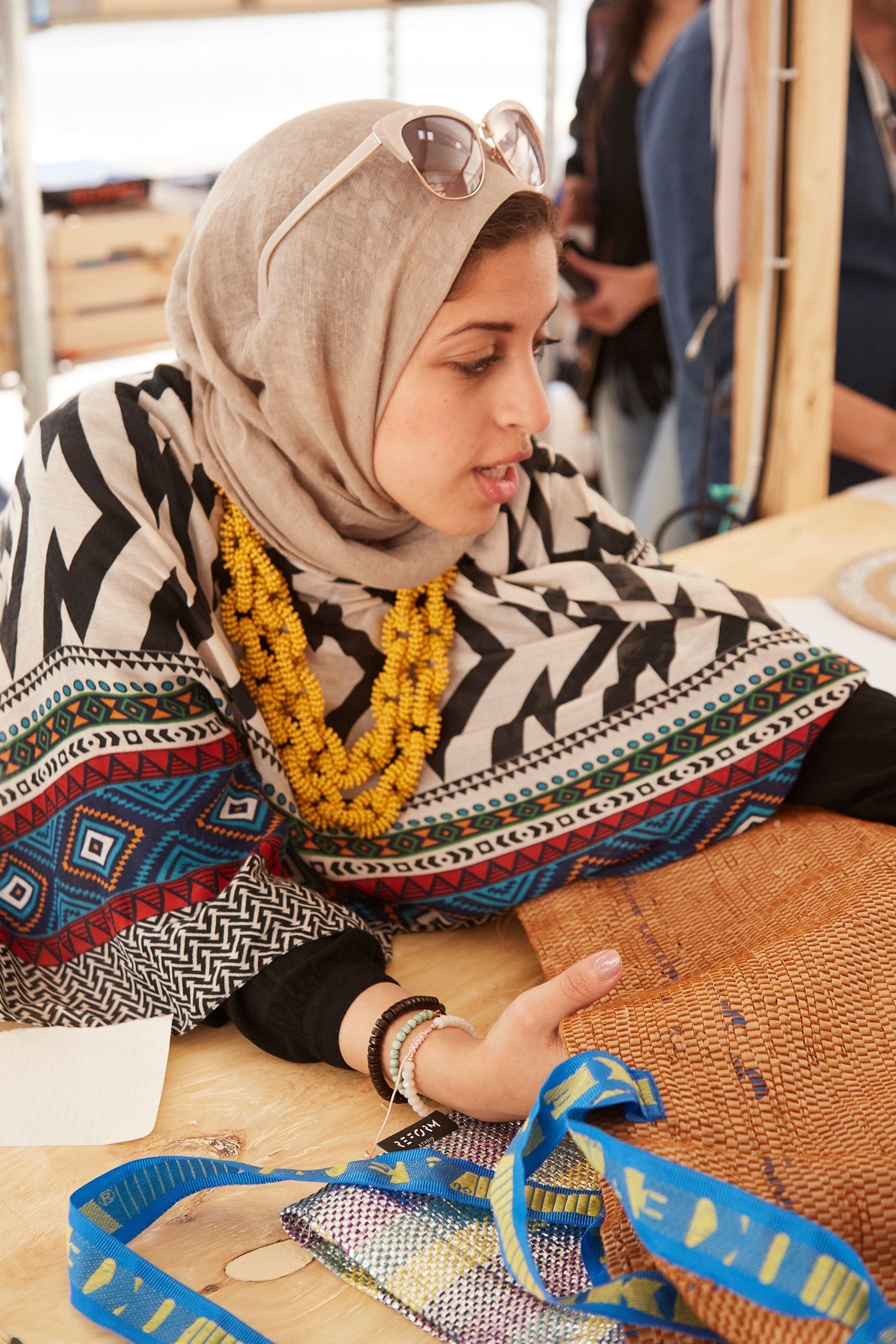 A woman looks at a piece of woven fabric. She has a bold yellow necklace.