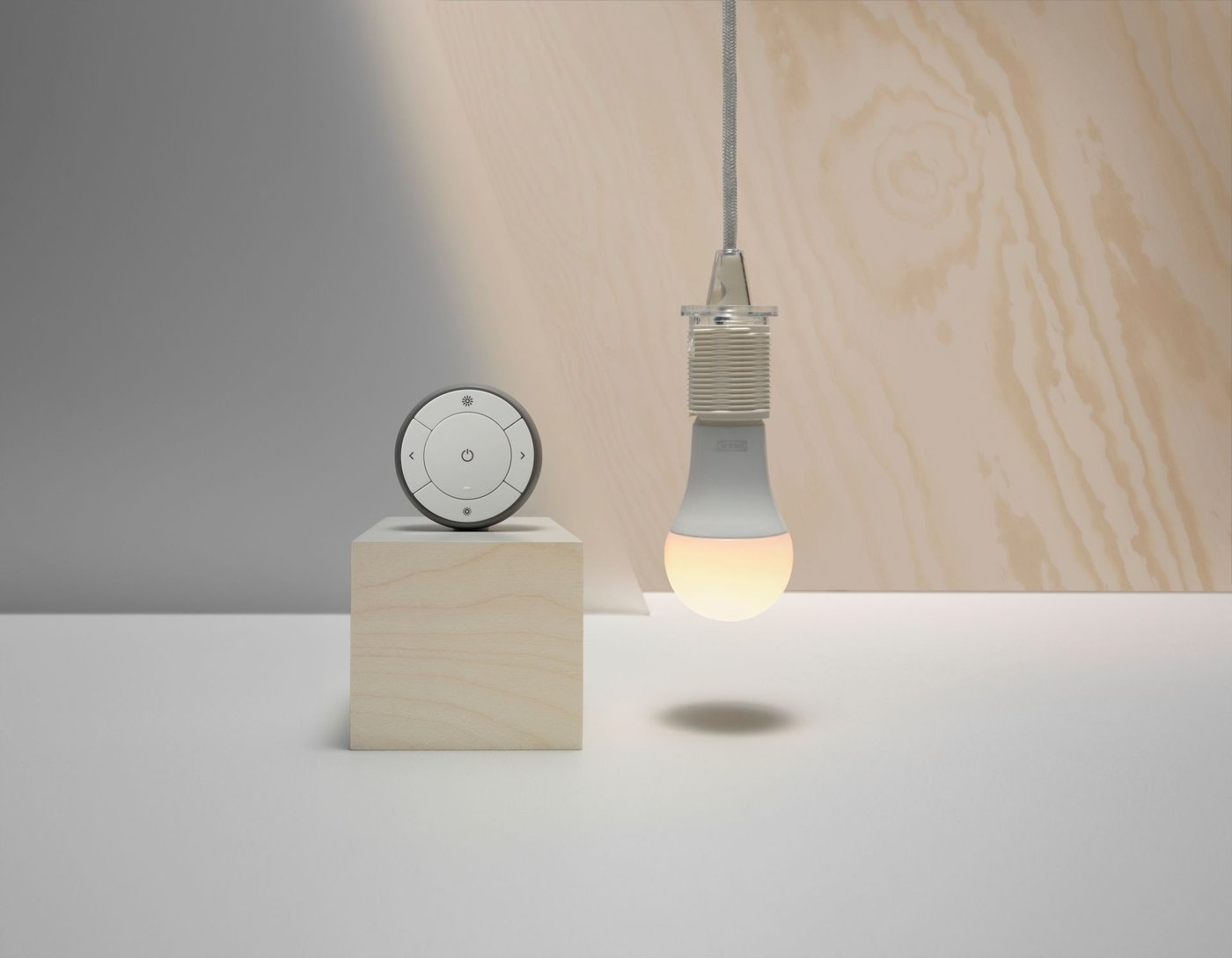 A clock on a plinth next to an illuminated light bulb hanging down.