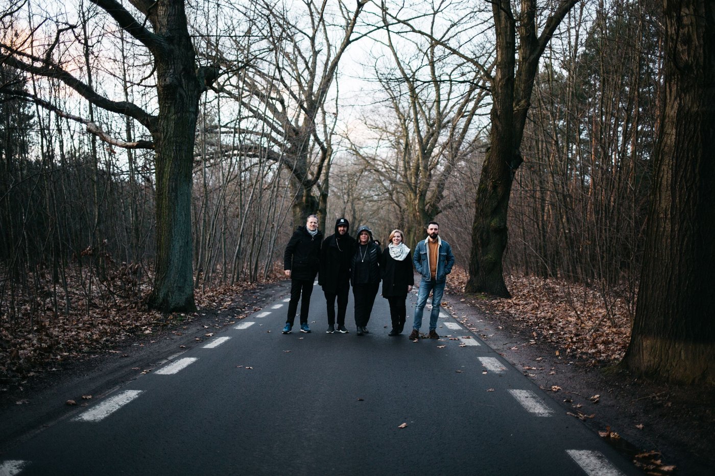 A group of people stand in a street surrounded by trees with fallen leaves.