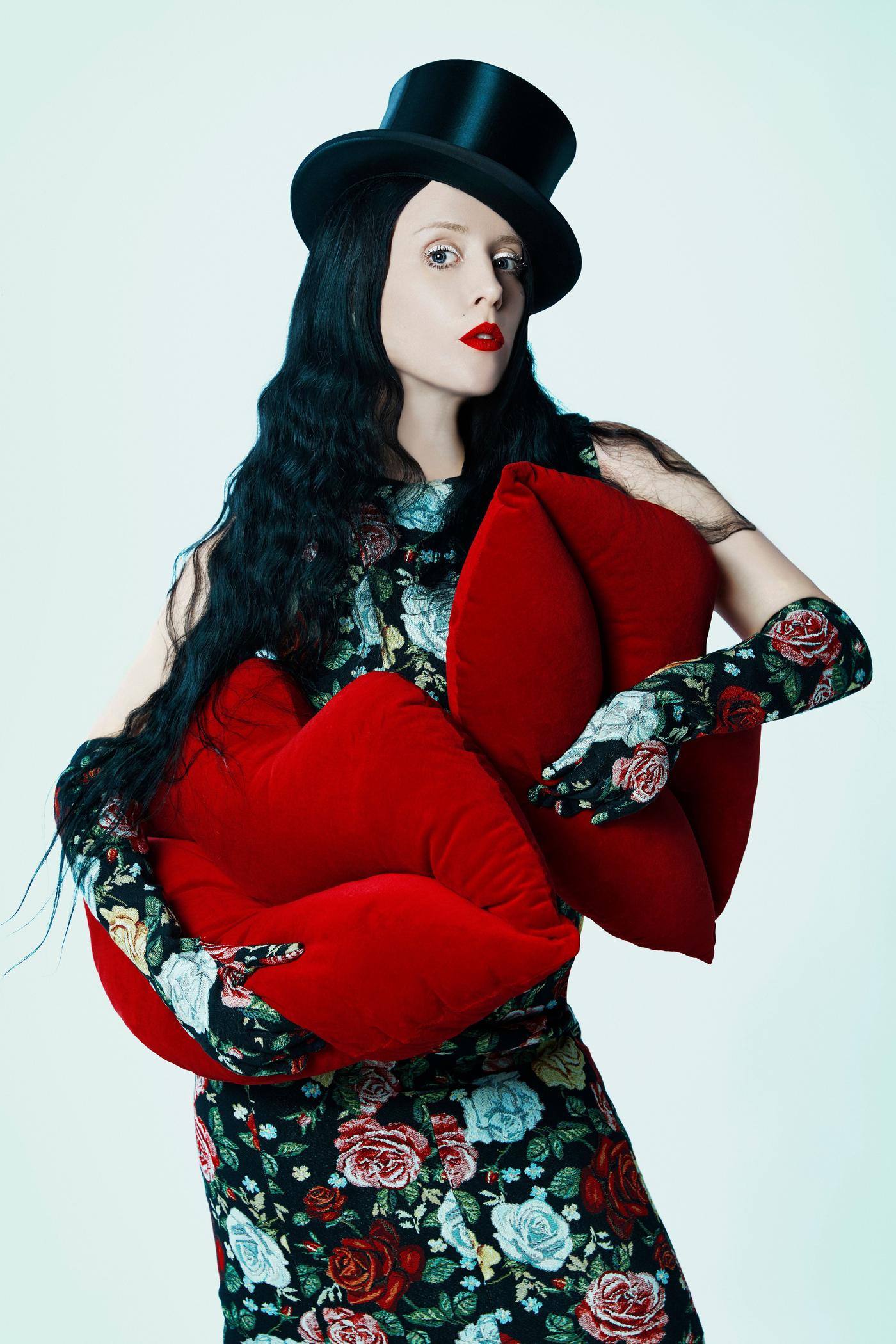 A woman in a black top hat holds two lip shaped cushions.