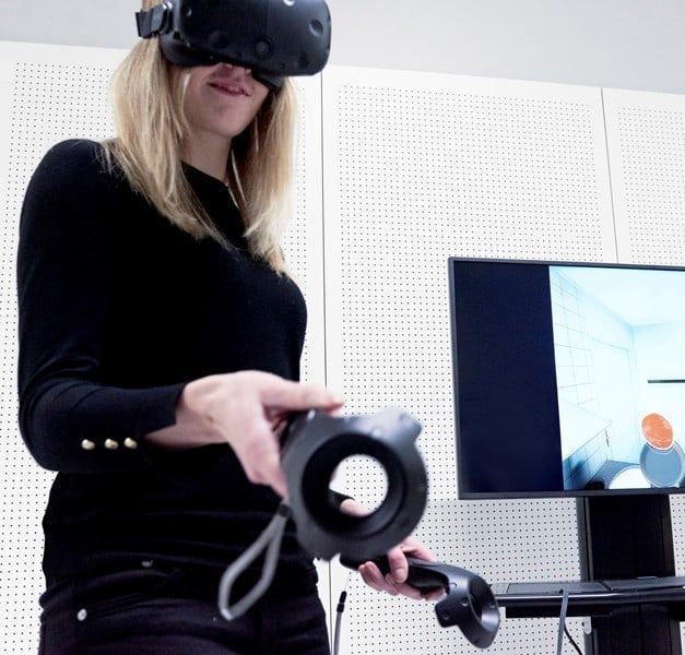 A woman is wearing virtual reality goggles. She is making a virtual pancake.
