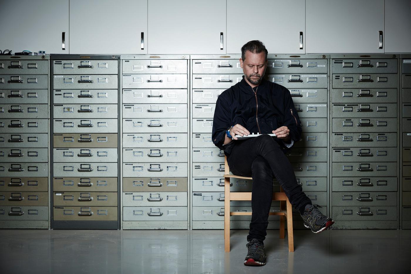 A man sits on a chair in front of a wall.