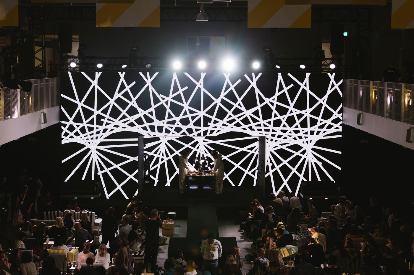 A room with people, screens with graphic designs and bright lights.