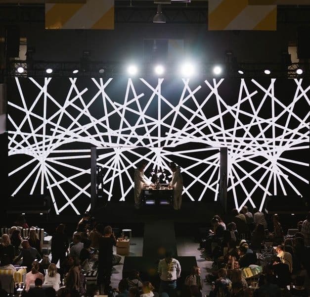 A room with people, screens with graphic designs and bright lights.