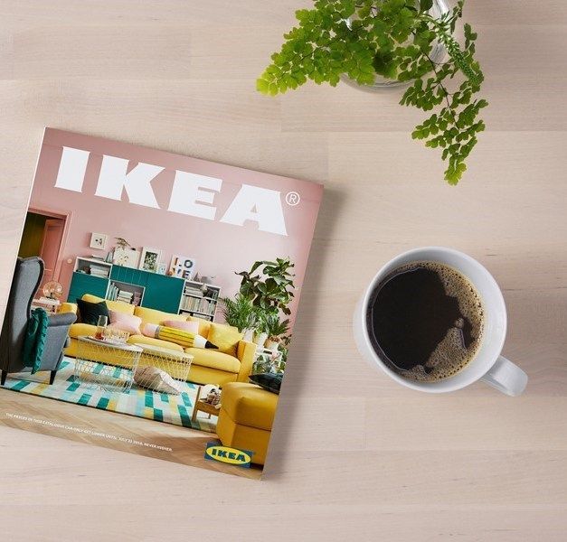 A wood surface with the 2018 IKEA Catalogue and a cup of hot beverage.