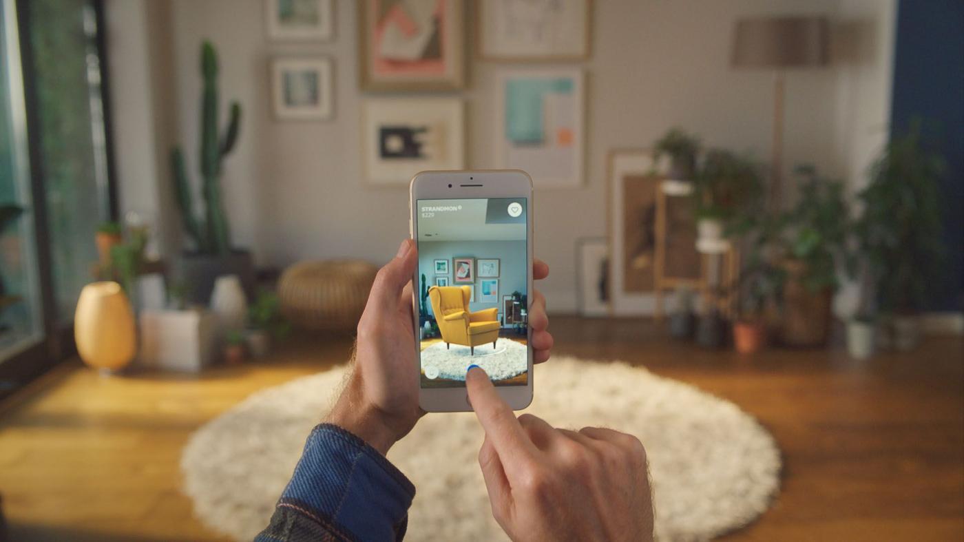 Hands holding a phone in a living room, interacting with the IKEA Place app.