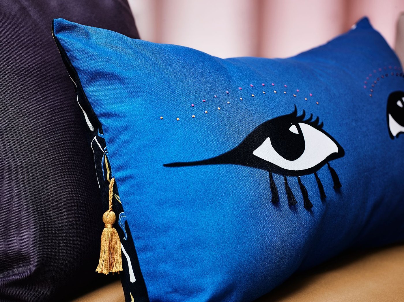A blue cushion with a pair of eyes and a tassle.