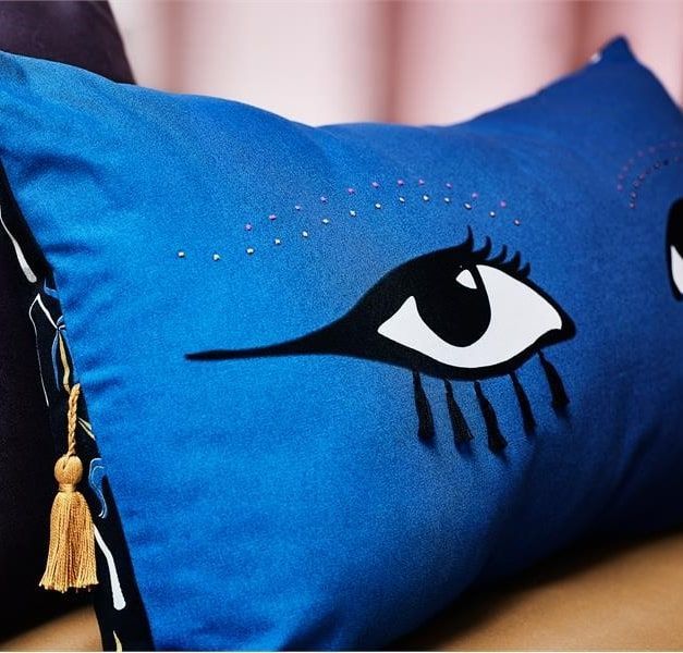 A blue cushion with a pair of eyes and a tassle.