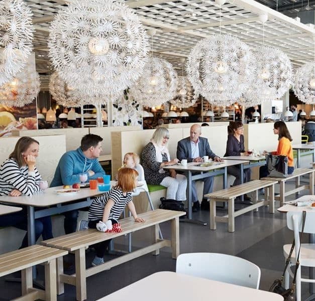 Diners eating at an IKEA restaurant with large pendant lamps suspended over the tables.