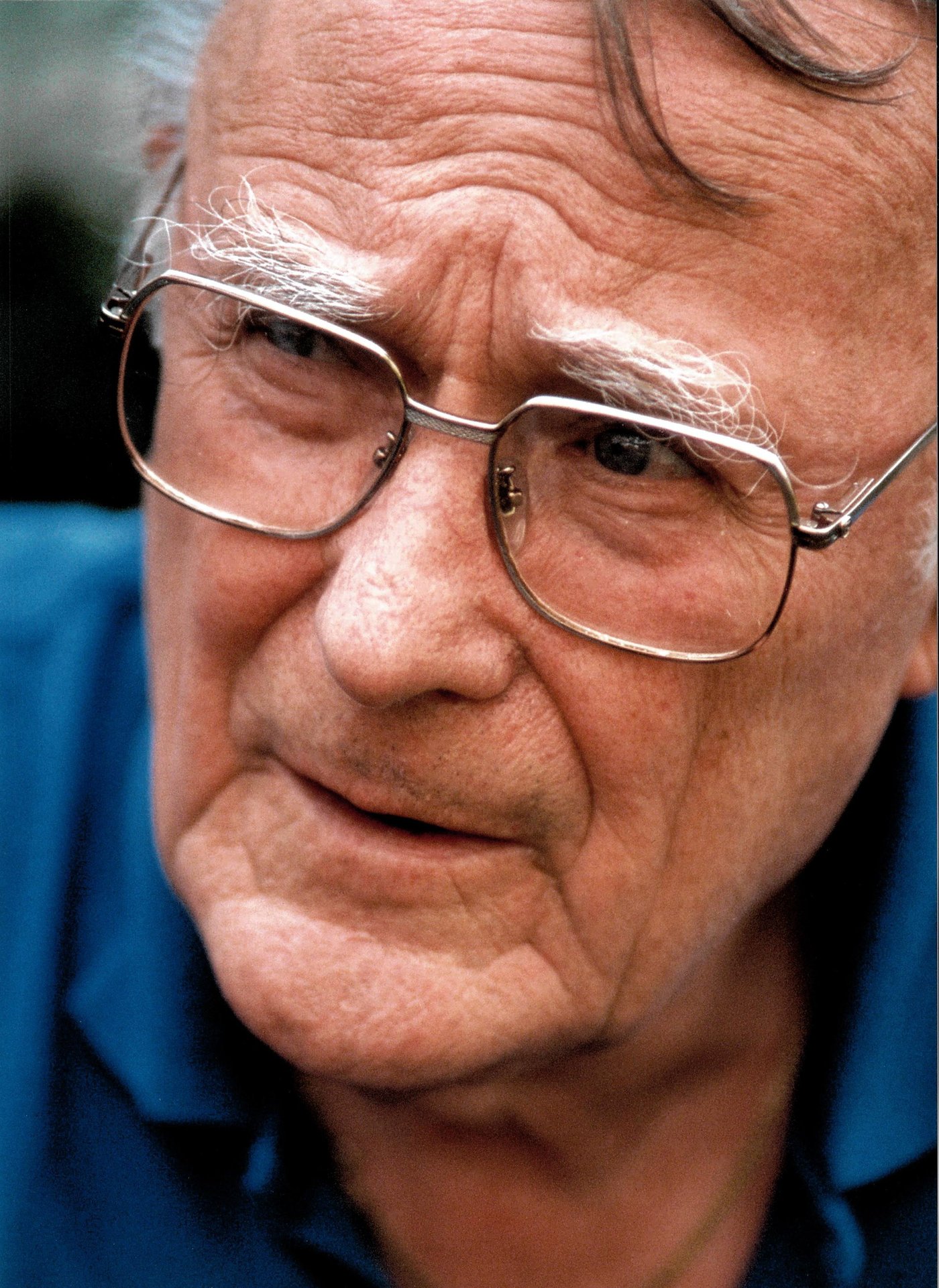 Close up of Ingvar Kamprad, wearing a blue shirt and glasses and looking away.