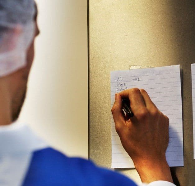 A person wearing a hairnet writes on a piece of notepaper on the wall.